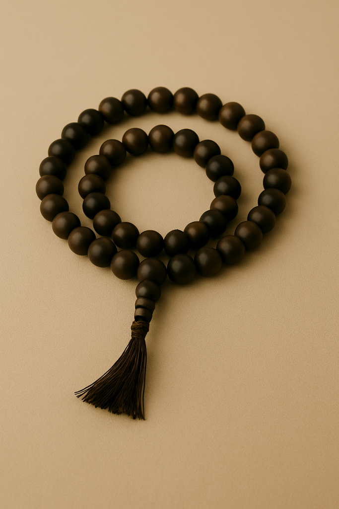 A looped string of dark wooden mala beads with a tassel, placed gently on a soft beige surface.